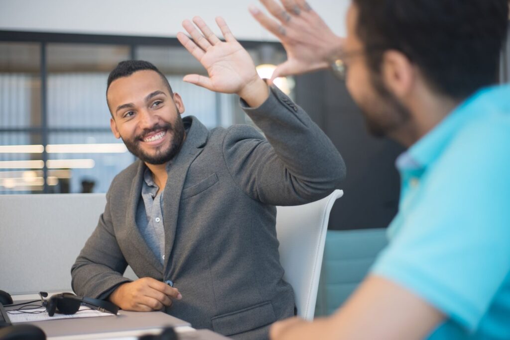 Two business professionals exchanging a high five, celebrating success in an office setting.